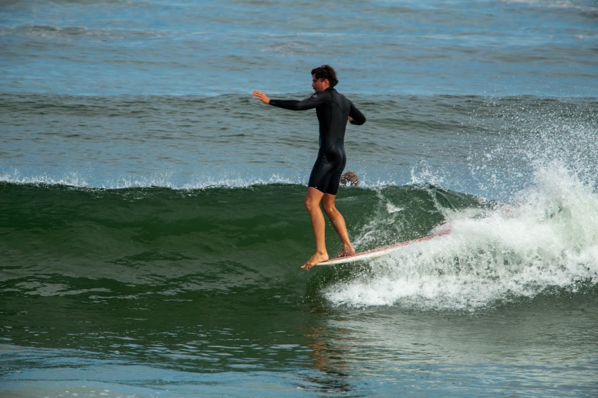 A surfer riding the face of a green wave with calm open water alongside