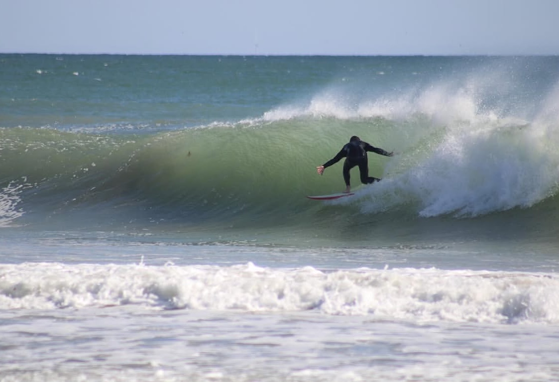 A surfer riding the clean face of a green wave beneath open sky and wide water